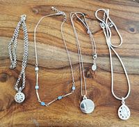 View of five silver-tone costume necklaces arranged side by side on a wooden surface, showing chain styles and pendants.
