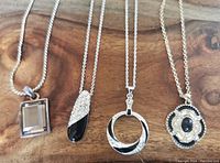 Four costume necklaces displayed with different pendant designs on a wooden surface.