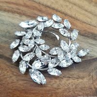 Front angle view showing marquise-cut clear rhinestones with silver-tone metal setting on a wood surface.