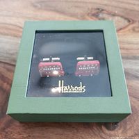 Pair of red London bus cufflinks in closed green Harrods box with clear lid and gold Harrods Knightsbridge logo.