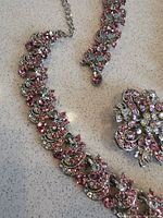 Close-up of necklace chain and part of brooch showing pink and clear CZ stones in ornate silver-tone metal