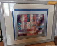 Full view of framed Yaacov Agam print showing damage on the top right corner of the grey frame with glass covering the art.