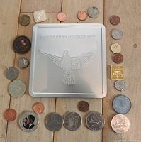 Overview of all coins arranged around silver tin box with embossed bird and Canadian commemorative dates.