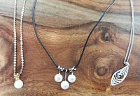 Front view of three necklaces laid flat on wood surface showing pearl details and chains.