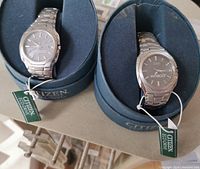Two watches in round blue velvet-lined Citizen Eco-Drive boxes with hang tags