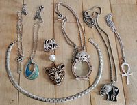 Photo showing six costume necklaces and one pendant with a slide arranged on a wooden surface, highlighting the various pendants with animal and symbolic motifs.