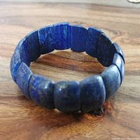 View of a stretch bracelet showing rectangular lapis lazuli beads with blue color and gold flecks, placed on wooden surface.