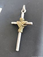 Close-up image of sterling silver cross pendant with gold wire wrapping on black background, showing front side