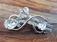 Close-up photo of sterling silver motorcycle-shaped brooch decorated with clear artificial crystals of various shapes on a wooden surface.