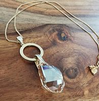 Close-up image of teardrop clear Swarovski crystal pendant on gold-tone circular ring with gold-tone chain on wooden surface.