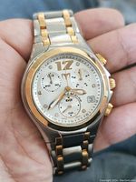 Close-up of TechnoMarine chronograph watch held in hand showing silver dial with gold accents, subdials, date window, and two-tone bracelet.