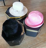 Three vintage hats on their original hat boxes; white, pink, black hats shown from top angle.