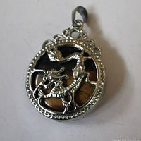 Front view of the circular tiger's eye pendant with silver dragon inlay and decorative frame.