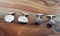Two pairs of sterling silver cufflinks side by side on wooden surface: engraved oval pair and knot pair.