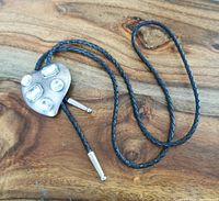 Full view of black braided leather bolo tie with guitar pick shaped silver-tone metal slide and clear gemstones.