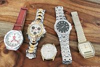 Five wristwatches laid out on wooden surface, showing various styles and conditions