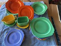 Set of colorful 1930s Homer Laughlin Rivera dishes laid out on a blue towel, including various plates, bowls, creamer, and sugar dish.