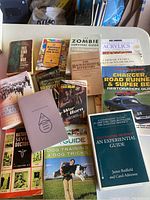 Photo showing full spread of 16 mixed genre paperback books laid out on a white surface, visible titles cover history, survival, art, fiction, and pets.