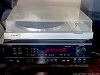 Sony turntable on top of a Denon AV surround receiver, showing the dust cover and part of the receiver front panel.