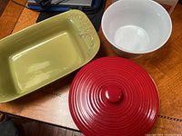 Three bake and serve dishes including a rectangular olive green dish, a white round bowl, and a red round lidded dish.