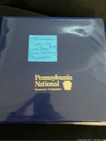 Blue three-ring binder with gold Pennsylvania National Insurance Companies logo and handwritten note listing Topps set and key players.