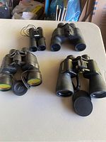 Lot of four binoculars arranged on table, showing varying sizes and lens styles.
