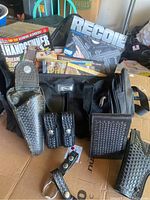 Overview photo showing the black leather holster, magazine pouch, wallet, small duffel bag, and firearm periodicals