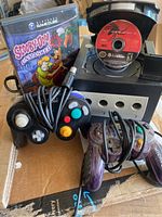 Nintendo GameCube console with two controllers, memory card, Scooby-Doo Unmasked game case, Spider-Man 2 game disc in console, and cords.