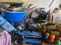 Wide view showing many camping and outdoor game items including bocce balls, horseshoes, a Coleman tent bag, cooler tub, and bow with arrows.