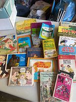Photo showing an assortment of vintage children's paperback books of various titles and styles spread on a table, including MAD magazine books and storybooks.