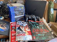 Photo showing stacked PS4 game cases including Medievil, Horizon Zero Dawn, Star Wars Battlefront II, Skyrim Special Edition, Resident Evil Village, and more, along with gaming magazines and two PlayStation 4 controllers in front of the console.