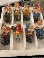 Top view of entire set showing seven different garden gnome figurines and mushroom cottage in protective styrofoam packaging, each wrapped in plastic.