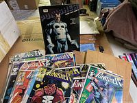 Overview photo showing the hardcover volume of The Punisher standing behind a spread of various vintage comic books from The Punisher series with different cover art.
