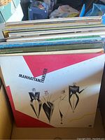 View of a stack of vintage vinyl records showing 'Manhattan Transfer' album on top with abstract geometric cover art.