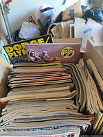 Stack of vintage automotive magazines and catalogs in box with visible Dodge Plymouth catalog and Moon Eyes catalog at top