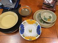 Photo showing a group of vintage dinnerware - various plates and bowls with distinct patterns and colors.