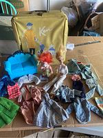 Vintage doll lot showing Ken wardrobe case, troll doll, Barbie doll in white outfit, Monster High style couch and assorted doll clothes on a table
