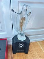 Baccarat crystal bird sculpture on black stand with logo and inscription on wooden floor.