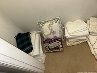View of folded blankets and linens on floor including plaid blanket, white blankets, and a boxed item labeled Dreamtime.