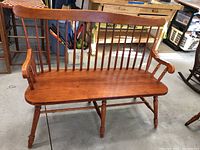 Front view of wooden bench with vertical spindle backrest, armrests, and turned legs.