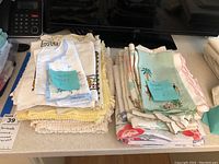 Two stacks of linens on a kitchen counter labeled Bermuda linens and tablecloths and napkins