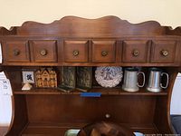 Wooden shelf with two metal book ends, two metal mugs, Asian decorative plate, and glass pyramid shown from front view