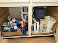 Overview of cleaning supplies stored under kitchen sink including detergents, sprays, sponges, and cleaning liquids.