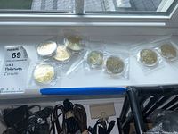 Coins individually sealed in plastic bags arranged on a windowsill and on a patterned carpet.