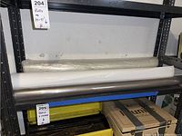 Three large commercial plastic rolls stacked on metal shelving, including clear, white, and dark rolls.