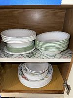 Photo of stacked white dinnerware and floral pattern plates inside a wooden cabinet shelf.
