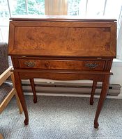 Front view of the wooden drop front secretary desk showing the closed drop-down writing surface and drawer with brass handles.