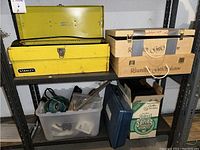 Shelf with a yellow Stanley toolbox, two wooden boxes, and a plastic container with tools and components below.