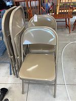 Four stacked beige metal folding chairs with rounded backrest, tubular metal legs, and flat seats.