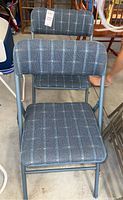 Photo of two metal folding chairs with gray padded upholstered seats and backrests in a geometric patterned fabric.